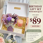 A birthday gift set being held open by a person, featuring a preserved flower bouquet wrapped in lavender paper, a pink scented candle, fairy lights, and a greeting card inside a white box. Promotional text on the right lists the set contents and price.