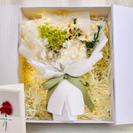 Detail shot of the green preserved hydrangea and dried floral bouquet inside the Eternal Glow Gift Box by Bloom and Forever, featuring white hydrangea clusters, green hydrangea, dried daisies, fluffy pampas grass, and rosemary, tied with a sage green ribbon