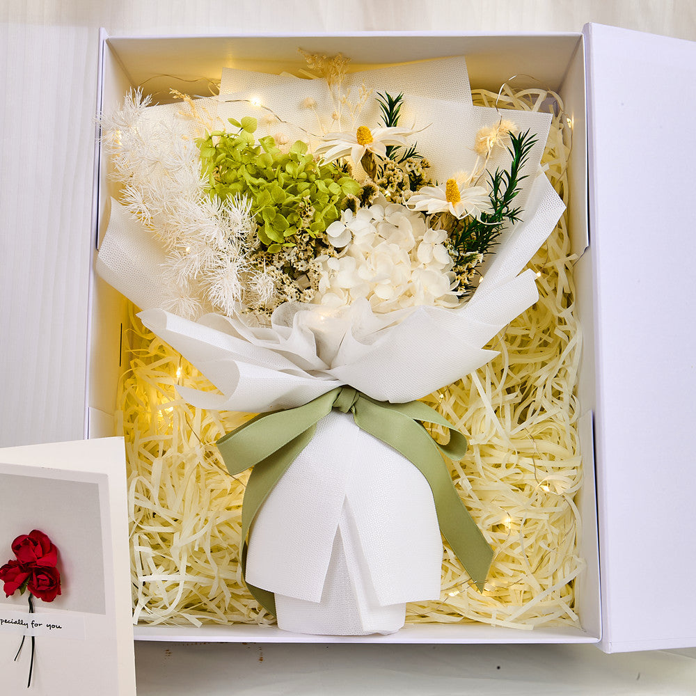 Detail shot of the green preserved hydrangea and dried floral bouquet inside the Eternal Glow Gift Box by Bloom and Forever, featuring white hydrangea clusters, green hydrangea, dried daisies, fluffy pampas grass, and rosemary, tied with a sage green ribbon