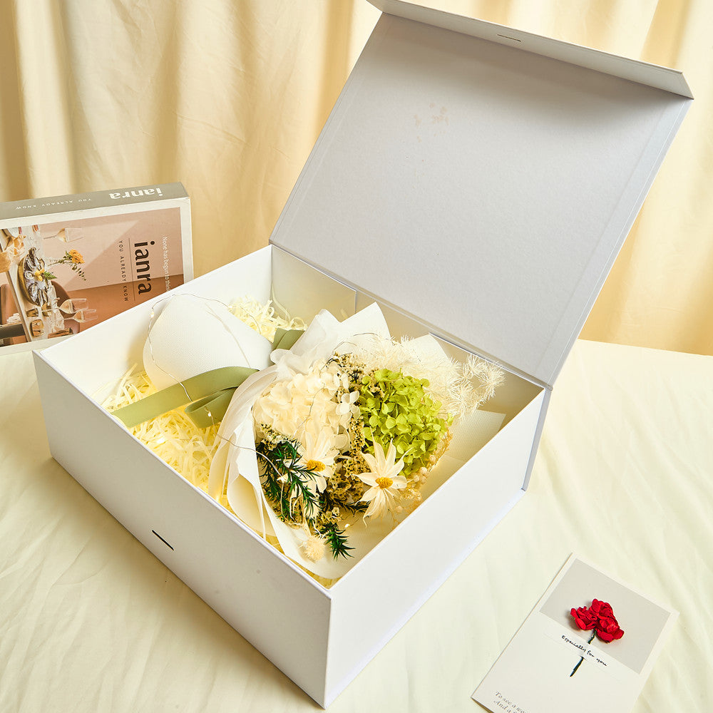 Side view of Bloom and Forever Eternal Glow Preserved Hydrangea Gift Box open on a cream surface, showing a green and white preserved hydrangea bouquet with sage green ribbon inside a white luxury gift box, with an Especially for You greeting card beside it