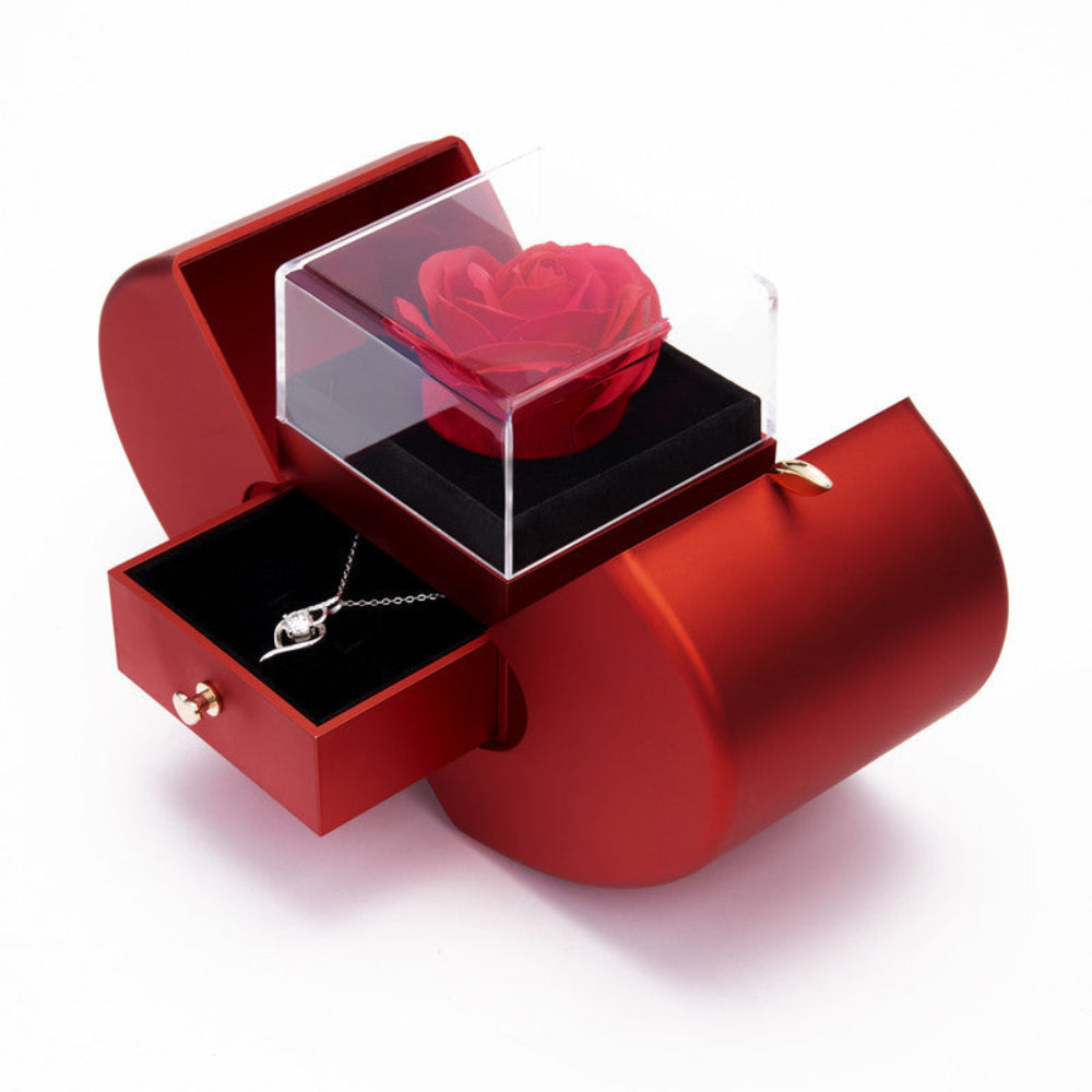 Bloom and Forever Eternal Rose Apple Jewelry Gift Box in red with apple-shaped doors open, showing a vibrant red preserved rose under a clear acrylic cover on a black velvet base, with the jewelry drawer pulled out revealing a silver crystal heart necklace inside, on a white background
