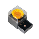 Bloom and Forever Eternal Sunflower Jewelry Drawer Box in grey with clear acrylic top, showing a vibrant yellow preserved sunflower under the lid and the jewelry drawer pulled open revealing a rose gold heart necklace inside the black velvet-lined drawer, on a white background