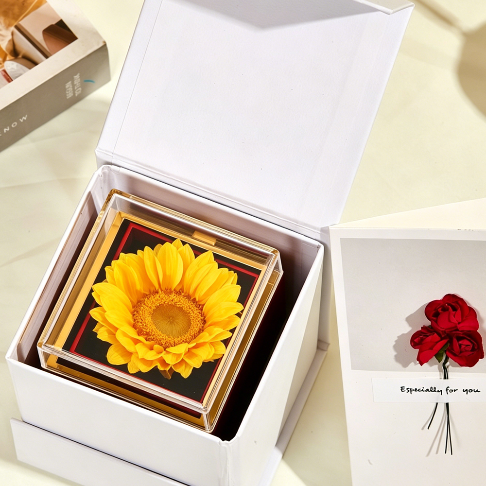 Bloom and Forever Eternal Sunflower Jewelry Drawer Box open inside a white outer gift box, showing a vibrant yellow preserved sunflower displayed under a clear acrylic lid on a black base with a red accent border, with an Especially for You greeting card beside it on a cream surface