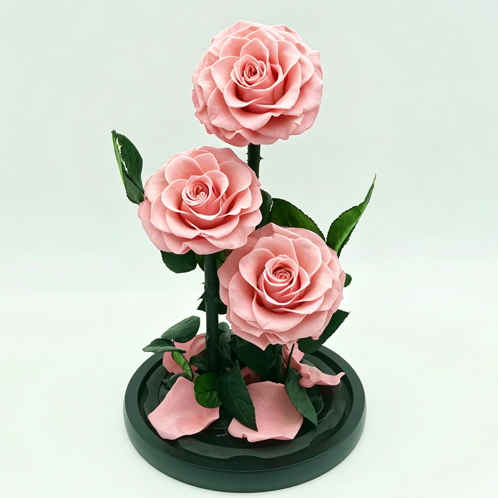 Three artificial pink roses with green leaves arranged on a round black base against a light gray background.
