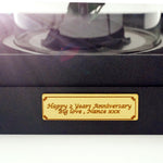 Close-up of a gold engraved personalised plaque on the black velvet base of a Bloom and Forever Everlasting Dome, displaying the custom message Happy 2 Years Anniversary Big love Nance xxx in elegant script, showcasing the bespoke personalisation option available for the Blush Hydrangea Everlasting Dome
