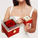 Woman wearing a silver moon and crystal necklace holding the open red Bloom and Forever Rotating Eternal Rose Jewelry Gift Box, showing a vibrant red preserved rose under the clear acrylic rotating lid with gold frame, and the jewelry compartment drawer pulled out revealing the necklace inside, on a white background